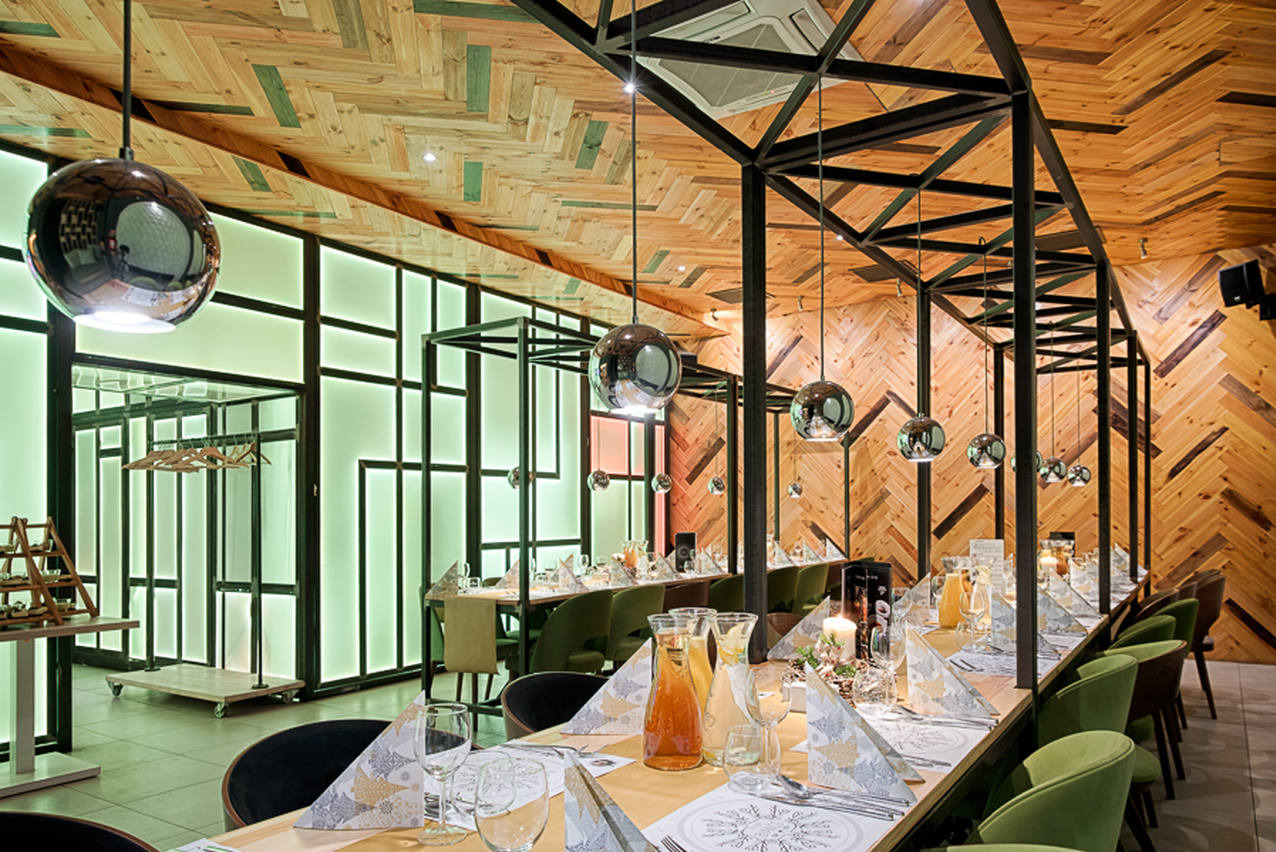 Uroczysta aranżacja stołu w nowoczesnej restauracji z drewnianymi ścianami w jodełkę i designerskimi lampami. Nakrycia, szkło i dekoracje tworzą elegancki klimat.