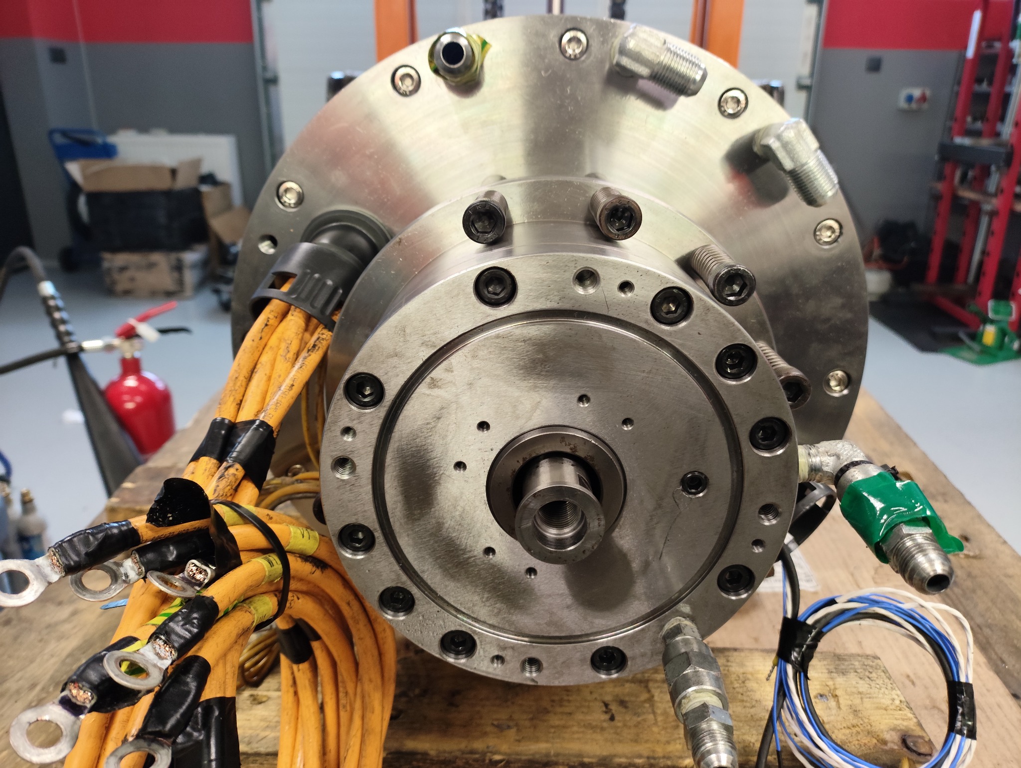 Elektrowrzeciono po regeneracji, widoczne przewody i elementy mocujące. Metalowa konstrukcja z licznymi śrubami i złączkami na drewnianym blacie.