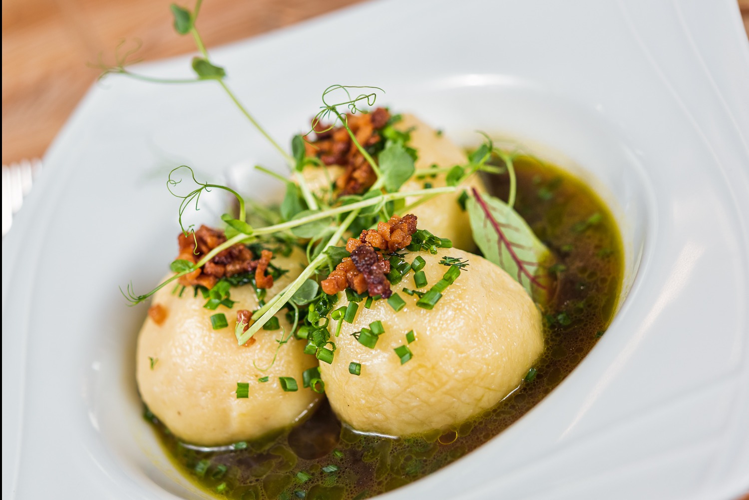 Elegancko podane kluski ziemniaczane w sosie, udekorowane zieleniną i skwarkami na białym talerzu. Danie gotowe do serwowania, z bliska.