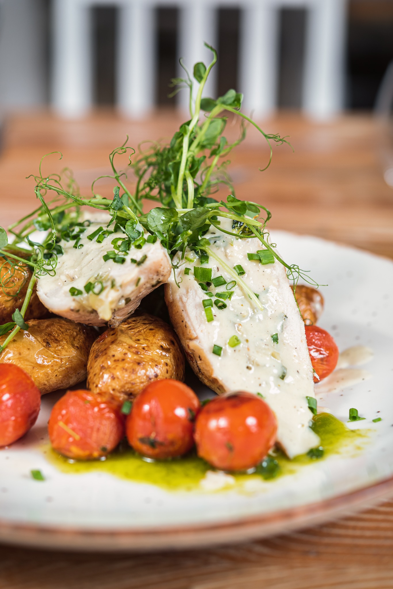 Elegancko podane danie z kurczaka w sosie, ziemniakami i pomidorami cherry, udekorowane zieleniną, serwowane na talerzu w restauracji w Łodzi.