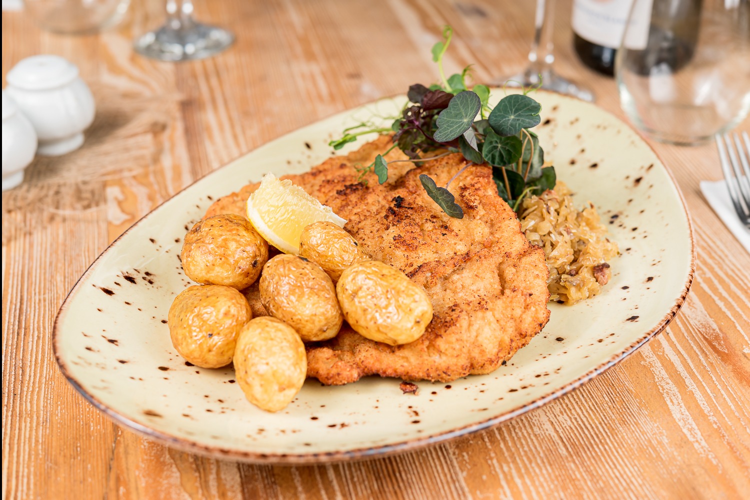 Apetyczny sznycel cielęcy z młodymi ziemniakami, kapustą i cytryną na ozdobnym talerzu, idealny na wykwintne przyjęcie.