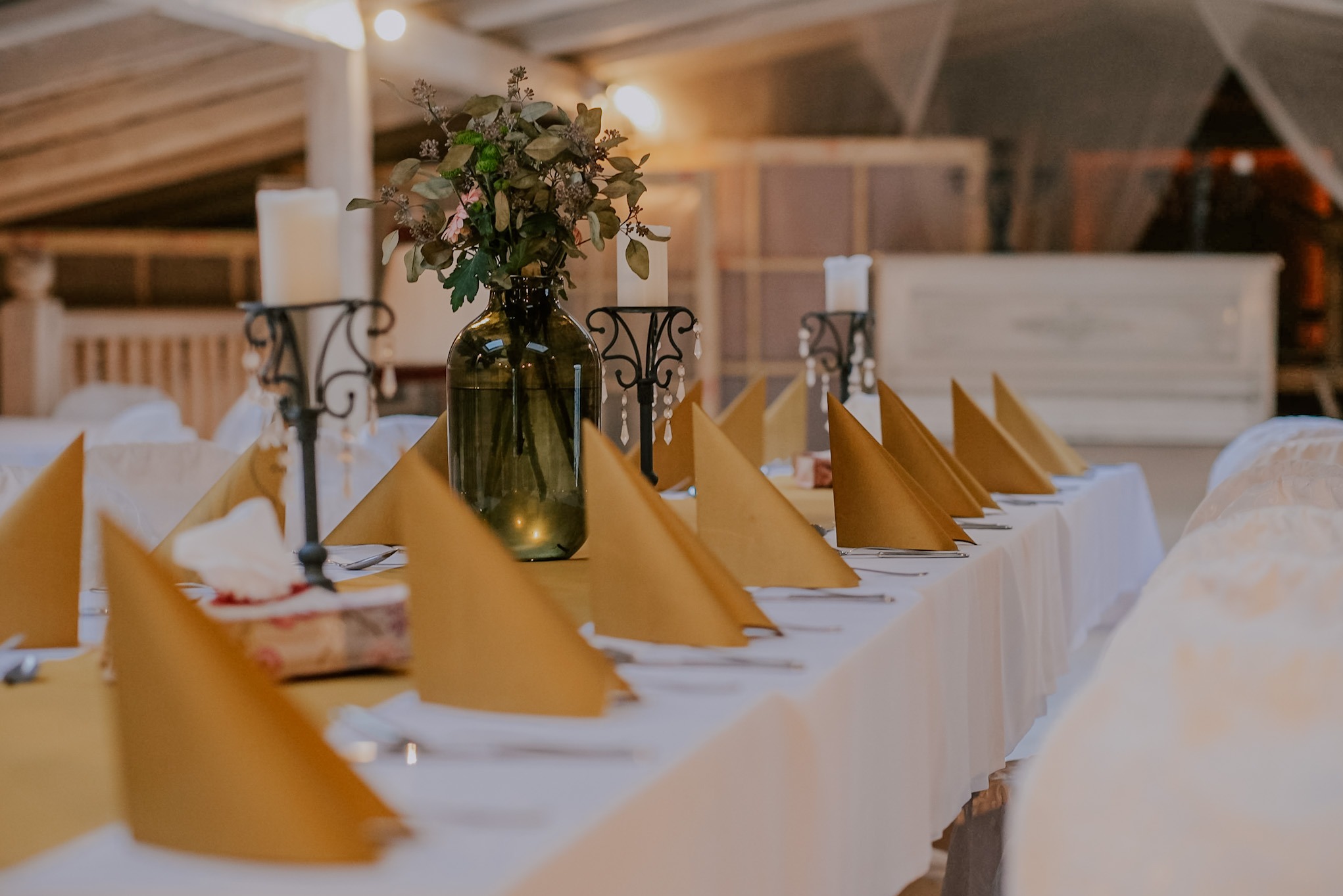 Dekoracja stołu z zielonym wazonem i złotymi serwetkami, świeczniki w tle. Ustawienie stołu na przyjęcie, elegancki wystrój, ciepłe światło.