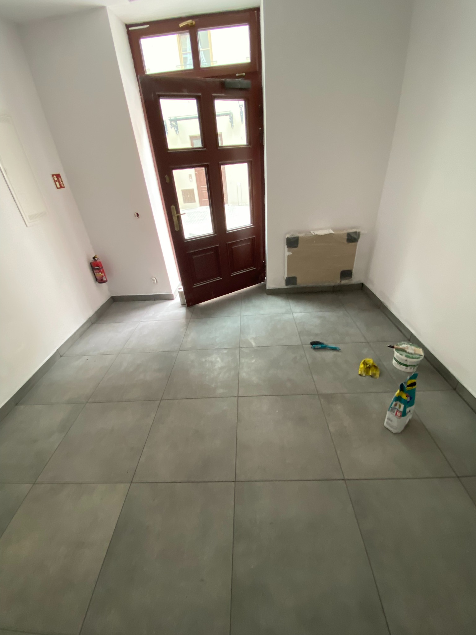 Ukończone płytki podłogowe w jasnym holu, z widoczną otwartą drewnianą stolarką drzwiową i narzędziami glazurniczymi. Ujęcie z góry.