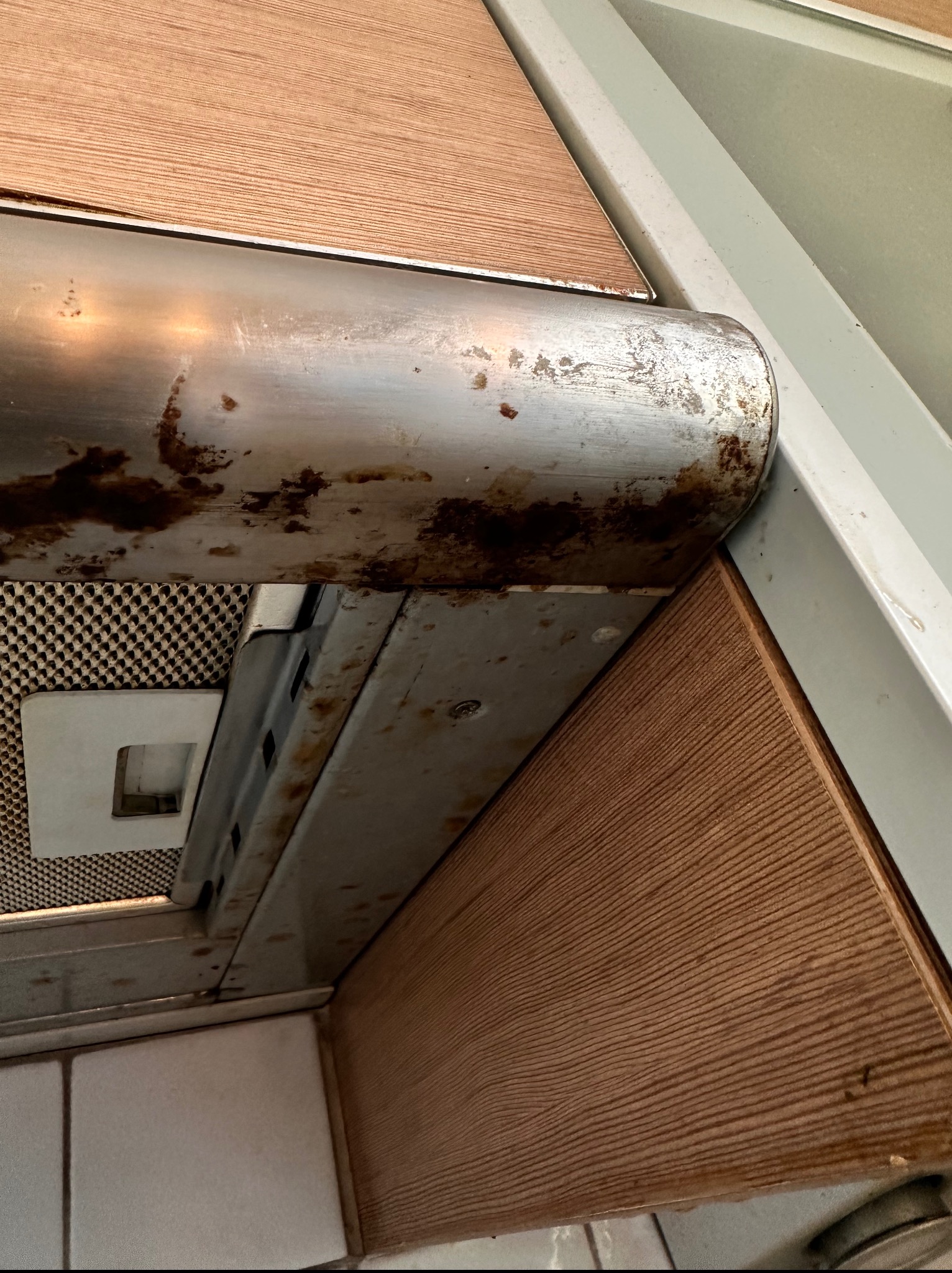 Silnie zabrudzony okap kuchenny z tłustymi plamami i osadem, widoczne filtry i metalowa obudowa. Konieczność gruntownego czyszczenia.