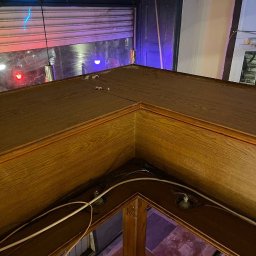 SUCCESS KID SPÓŁKA Z OGRANICZONĄ ODPOWIEDZIALNOŚCIĄ - Kąt widzenia na drewniany bar z widocznymi przewodami i elementami mocującymi, z roletą okienną w tle. Widok z góry na bar w lokalu.