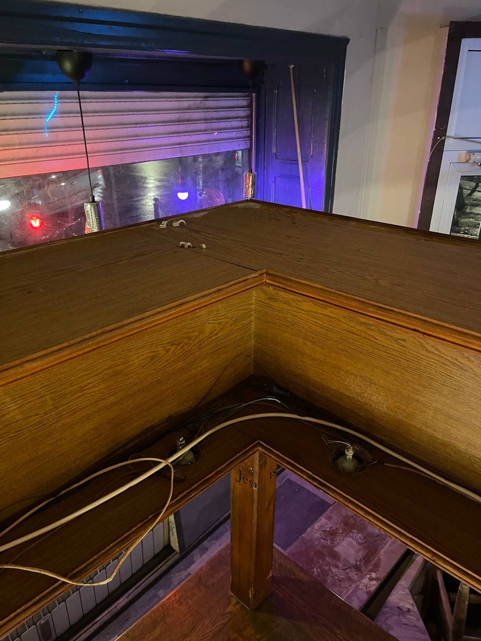 Kąt widzenia na drewniany bar z widocznymi przewodami i elementami mocującymi, z roletą okienną w tle. Widok z góry na bar w lokalu.