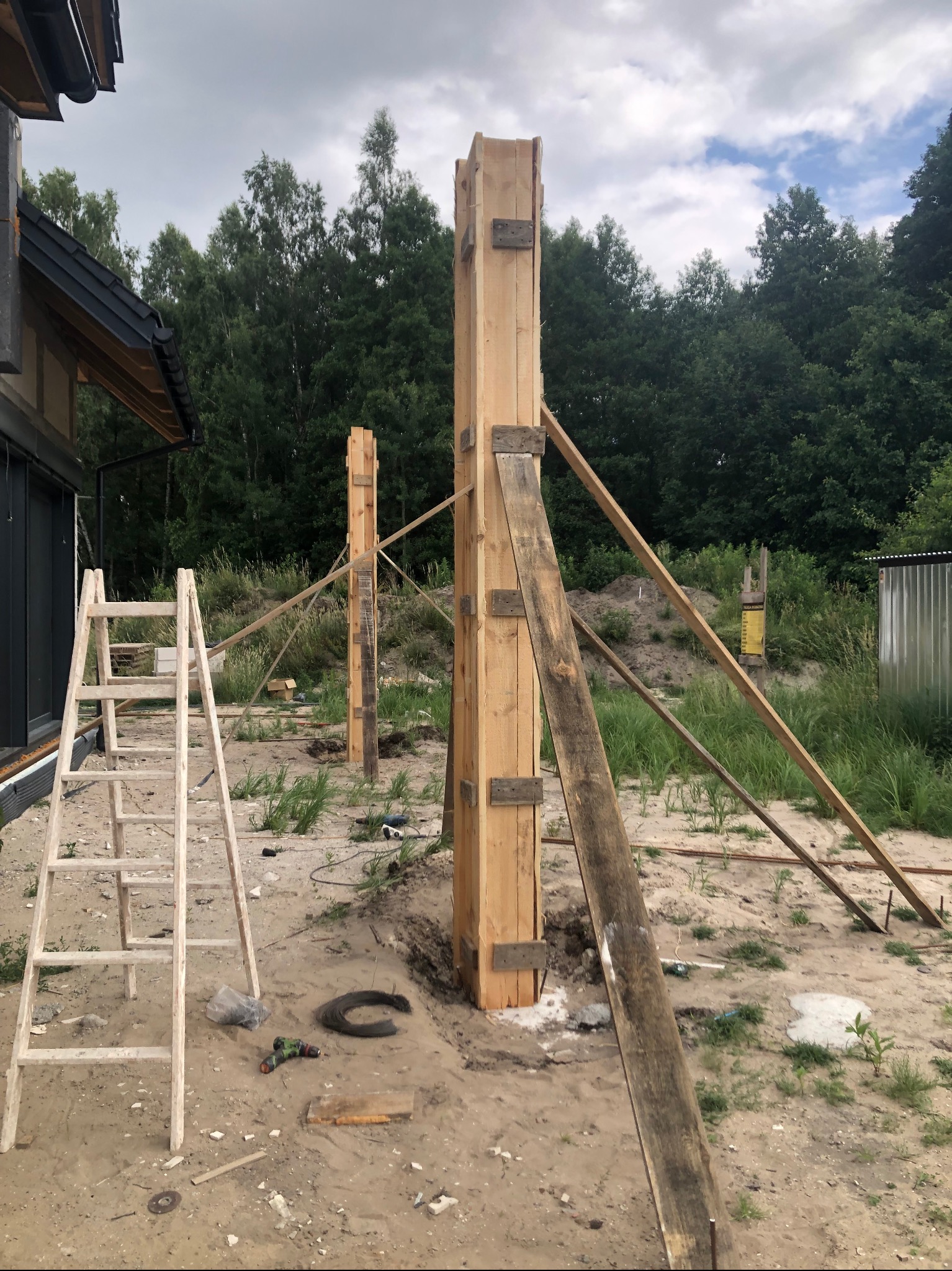 Przygotowanie szalunku pod betonowe słupy tarasu. Drewniane stemple podtrzymują konstrukcję. W tle zieleń i fragment domu.