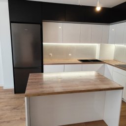 ROYAL MEBLE - Nowoczesna kuchnia z wyspą: białe szafki, czarne górne szafki, drewniany blat wyspy i duża lodówka Samsung. Oświetlenie LED pod szafkami.