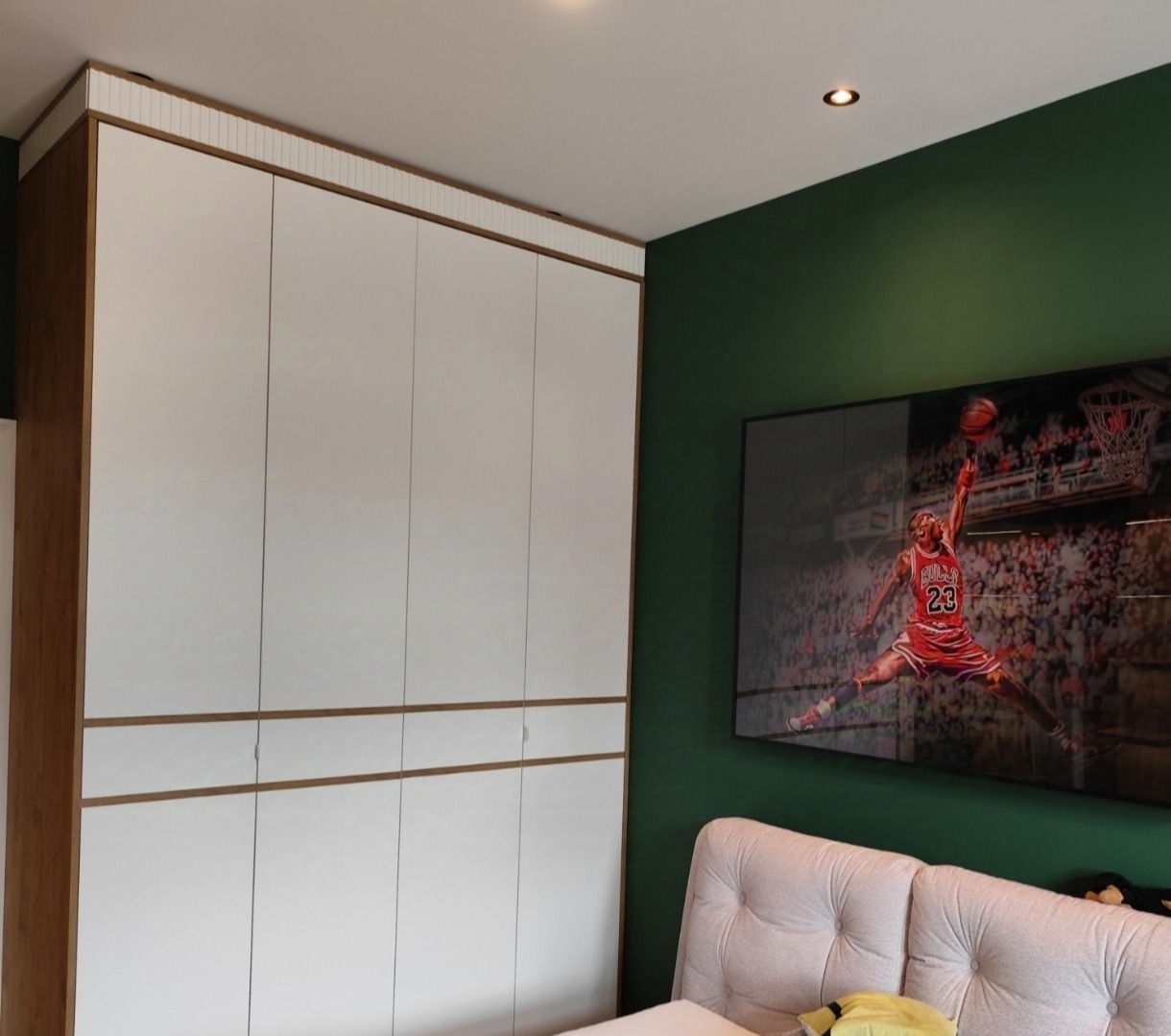 Biała szafa wnękowa z drewnianymi akcentami na tle zielonej ściany z telewizorem, na którym wyświetlany jest obraz Michaela Jordana.