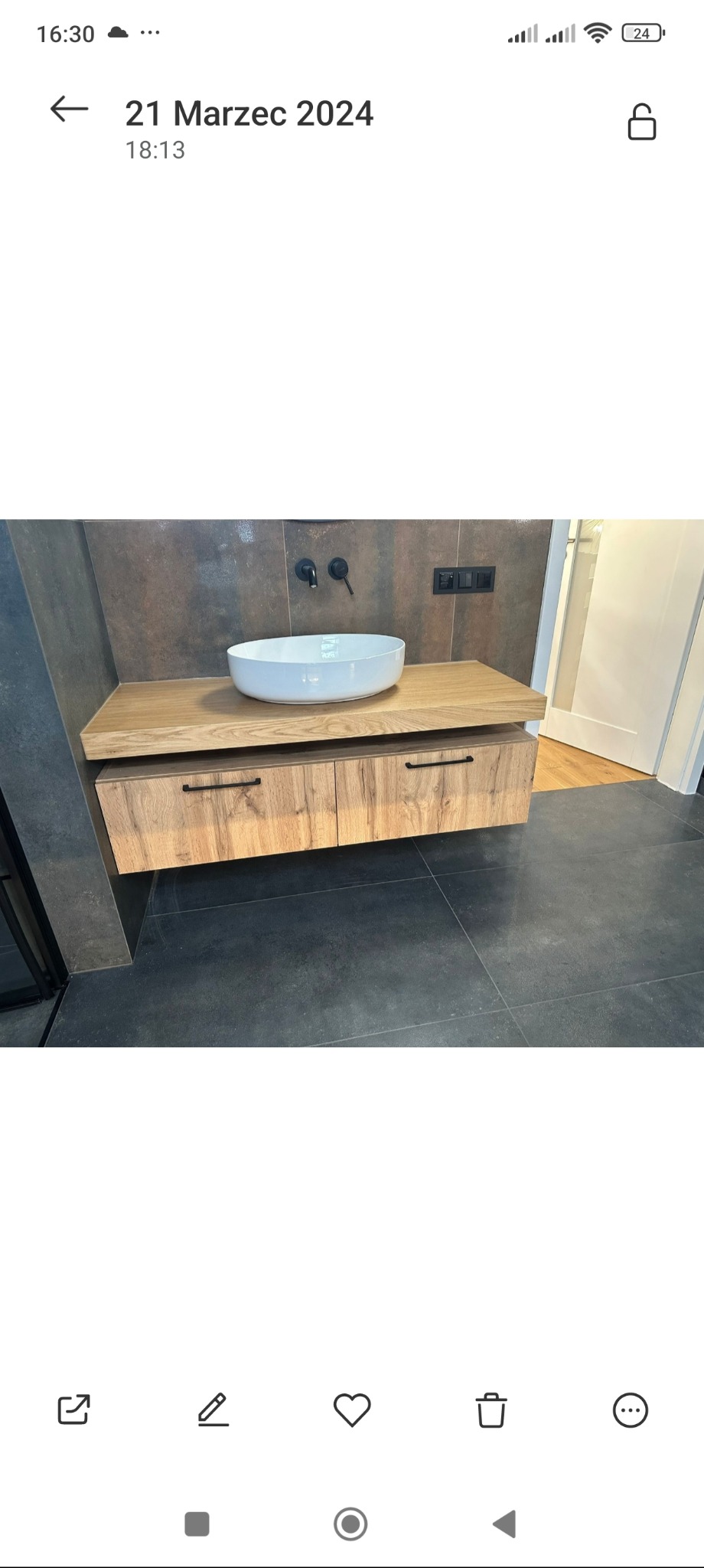 Nowoczesna łazienka z drewnianą szafką pod umywalkę nablatową i czarną armaturą, na tle ciemnych płytek. Minimalistyczny design z dbałością o detale.