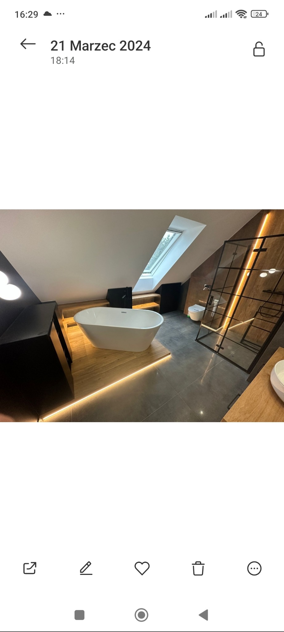 Elegancka łazienka na poddaszu z wolnostojącą wanną, drewnianym podestem z podświetleniem LED i kabiną prysznicową ze szprosami. Okno dachowe doświetla wnętrze.