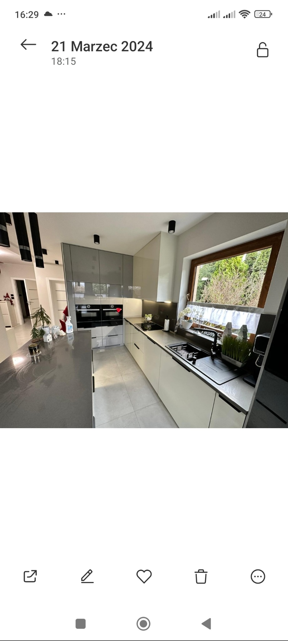 Nowoczesna kuchnia z szarymi i białymi szafkami, czarnymi akcentami i oknem z widokiem na zieleń. Blat z szarego kamienia, minimalistyczny design.