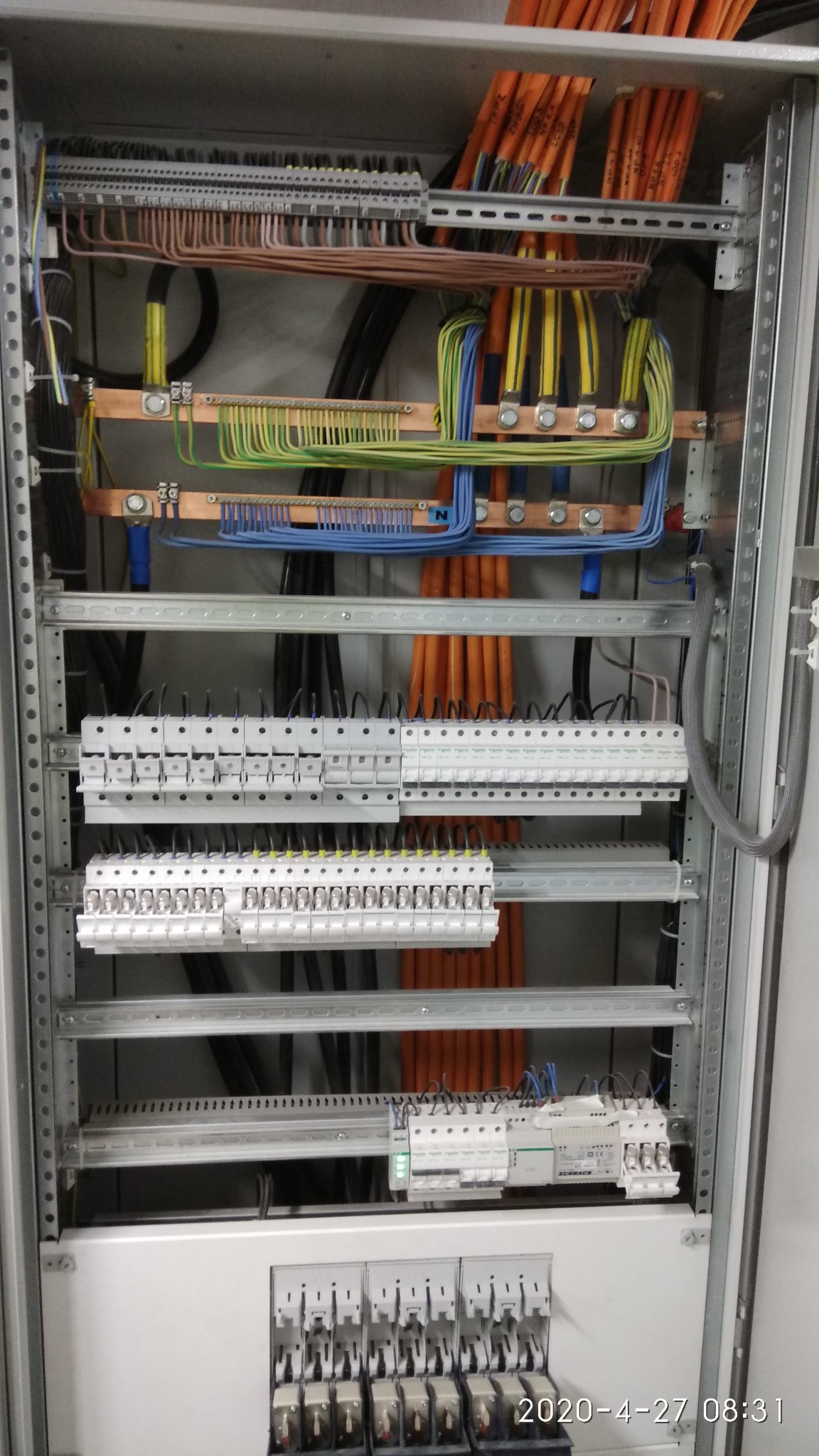 Rozdzielnia elektryczna w metalowej obudowie z licznymi przewodami, listwami zaciskowymi i zabezpieczeniami. Kable ułożone są równolegle i uporządkowane.