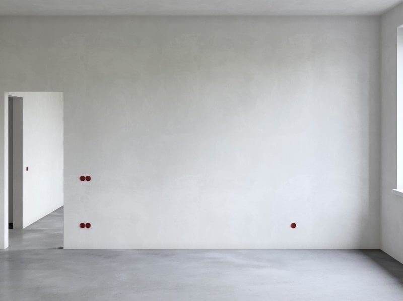 Jasne, puste wnętrze po gładziowaniu ścian i wylewce podłogi. Widoczne czerwone punkty instalacji elektrycznej i otwór drzwiowy w tle.