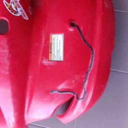 Czerwony plastikowy element z naklejkami (All Balls Racing, Monster) i czarnym szwem. Widoczne ślady użytkowania i ostrzeżenie o wadze ładunku.