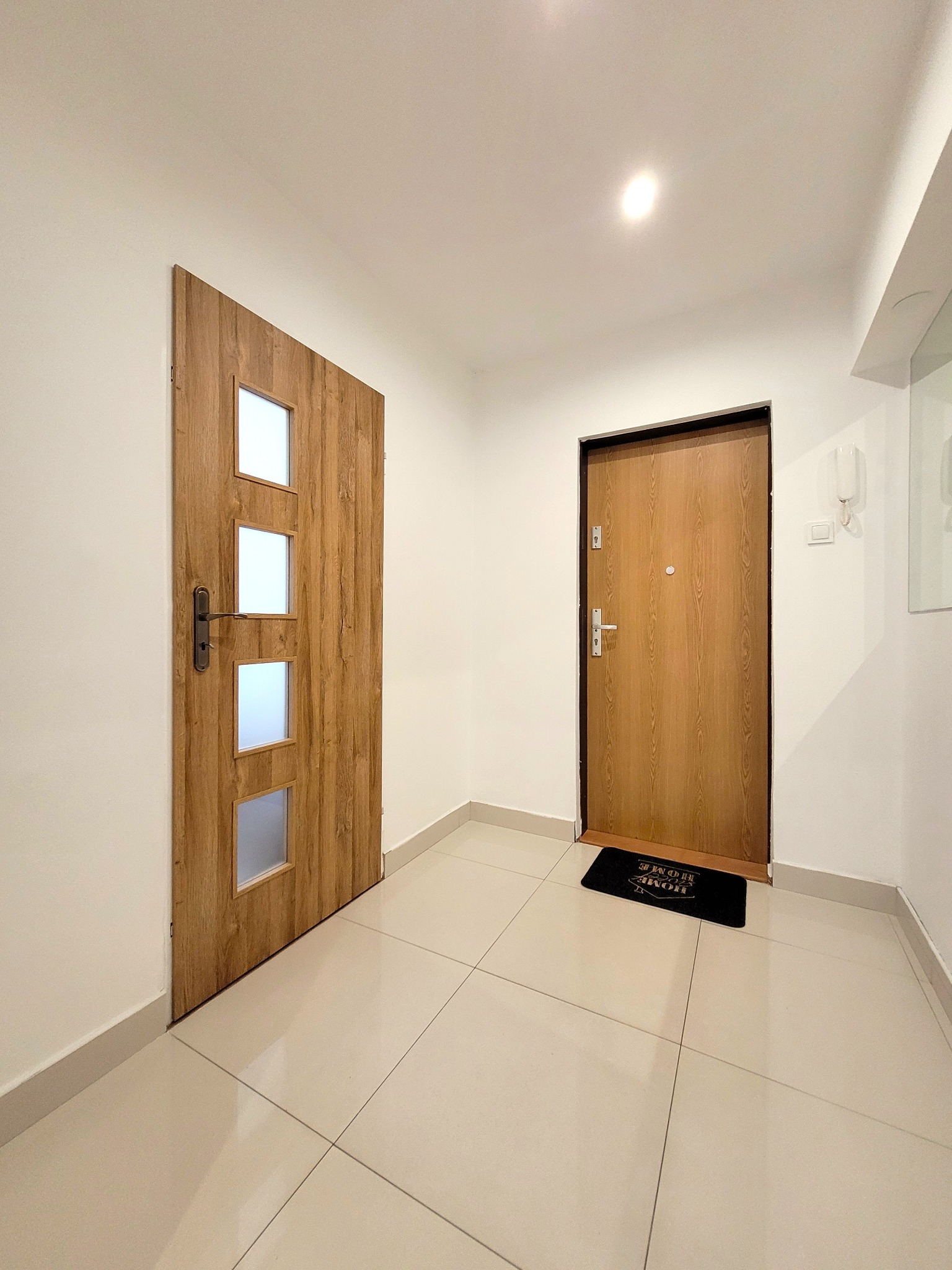 Jasne wnętrze mieszkania po odświeżeniu: białe ściany, beżowe płytki podłogowe, dwoje drewnianych drzwi. Nowoczesny design.