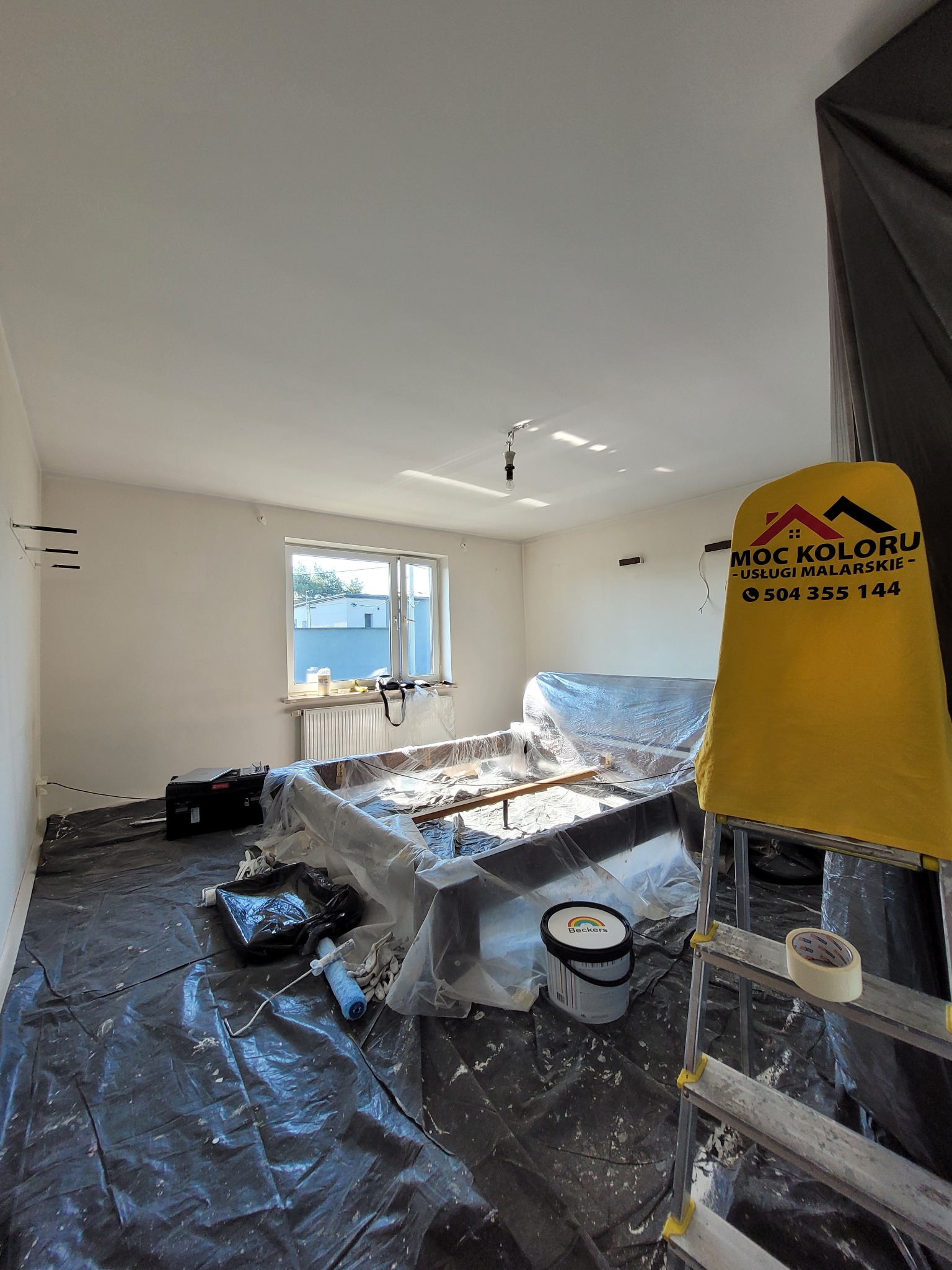 Pokój w trakcie malowania: zabezpieczone meble folią, rozłożona folia ochronna na podłodze, widoczna drabina z logo firmy malarskiej i puszka farby.