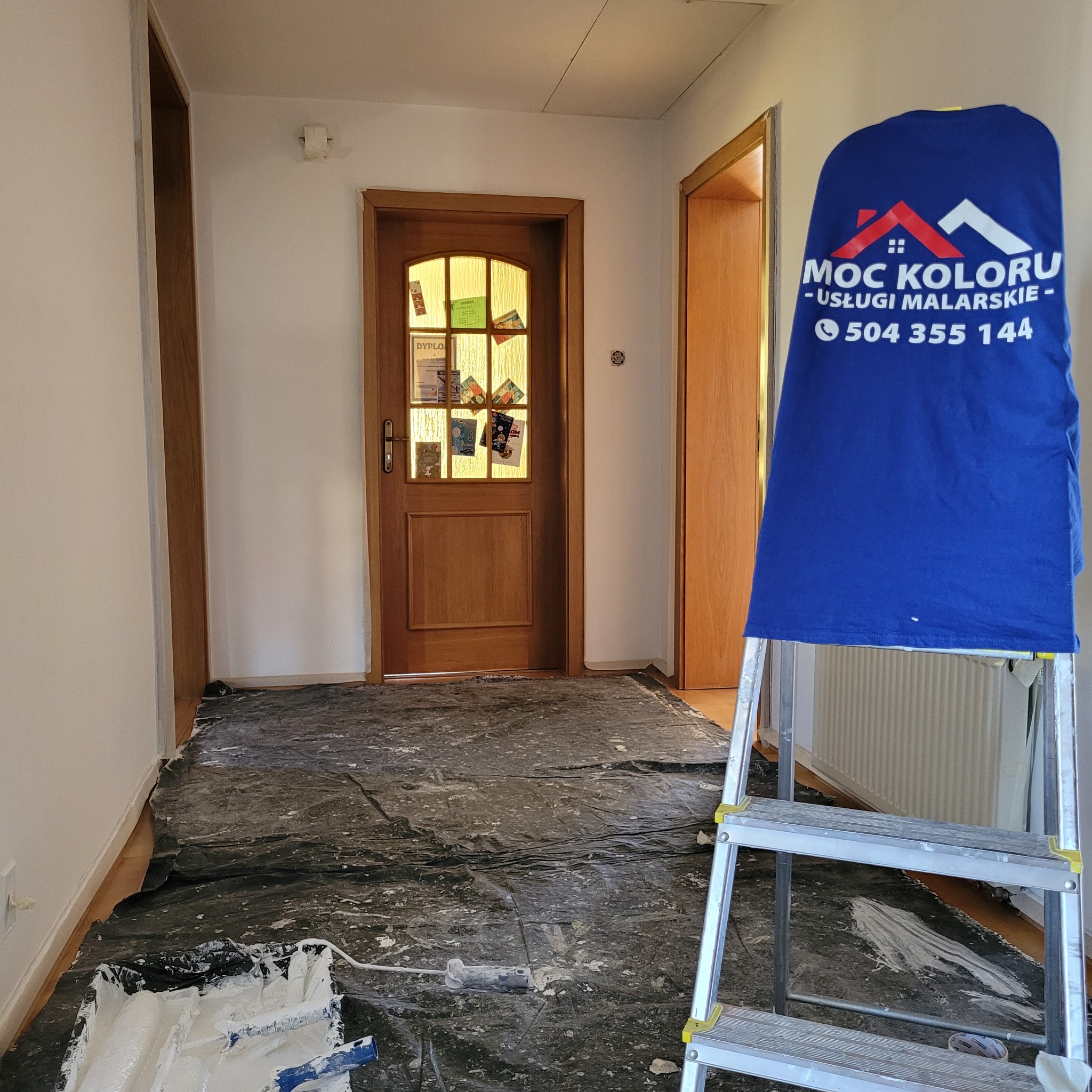 Korytarz w trakcie odświeżania: zabezpieczona podłoga, drabina z firmową koszulką, świeżo pomalowane ściany. Widoczne drzwi z dyplomami.