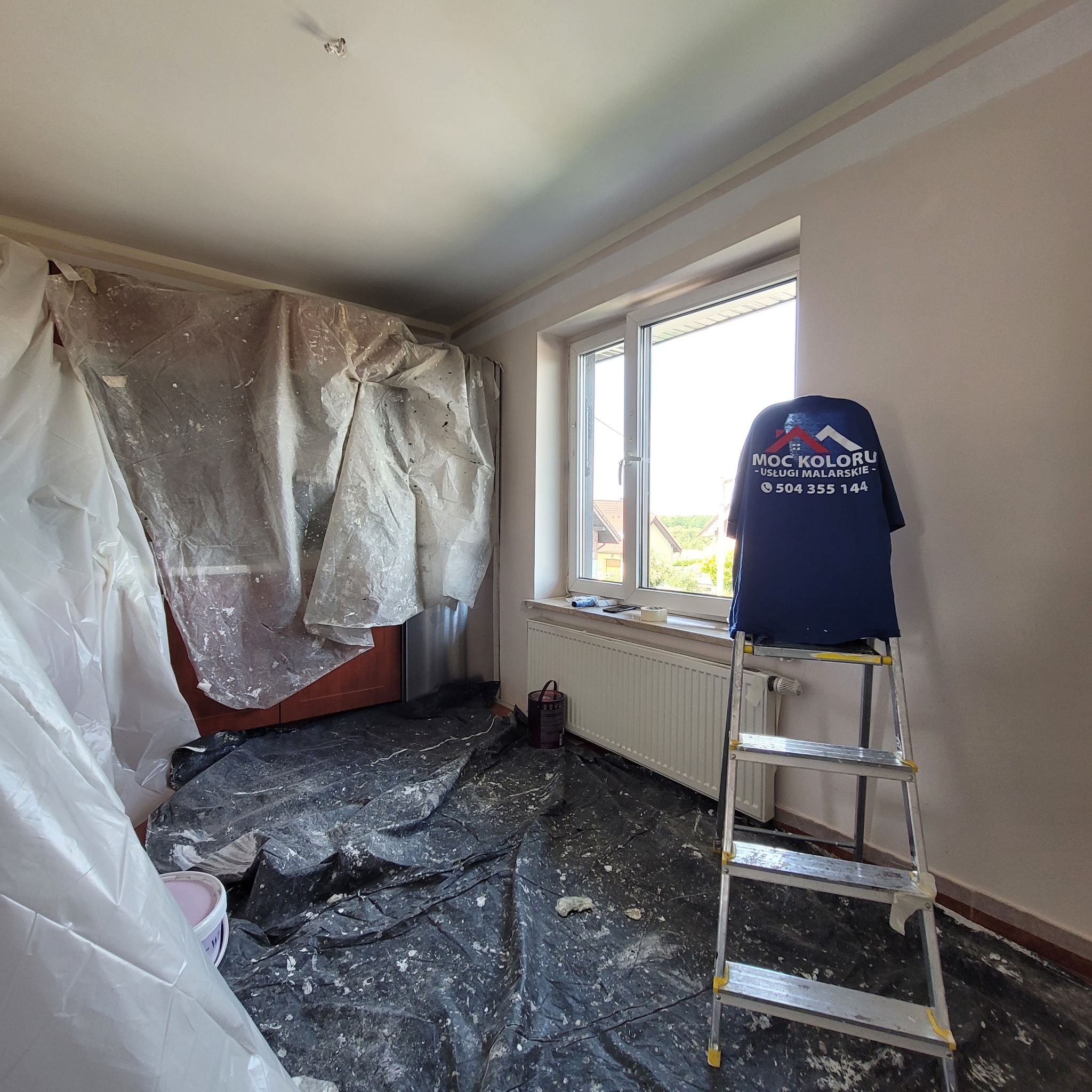 Pokój w trakcie zabezpieczania przed pracami malarskimi: meble okryte folią, rozłożona folia ochronna na podłodze, drabina z koszulką firmy.