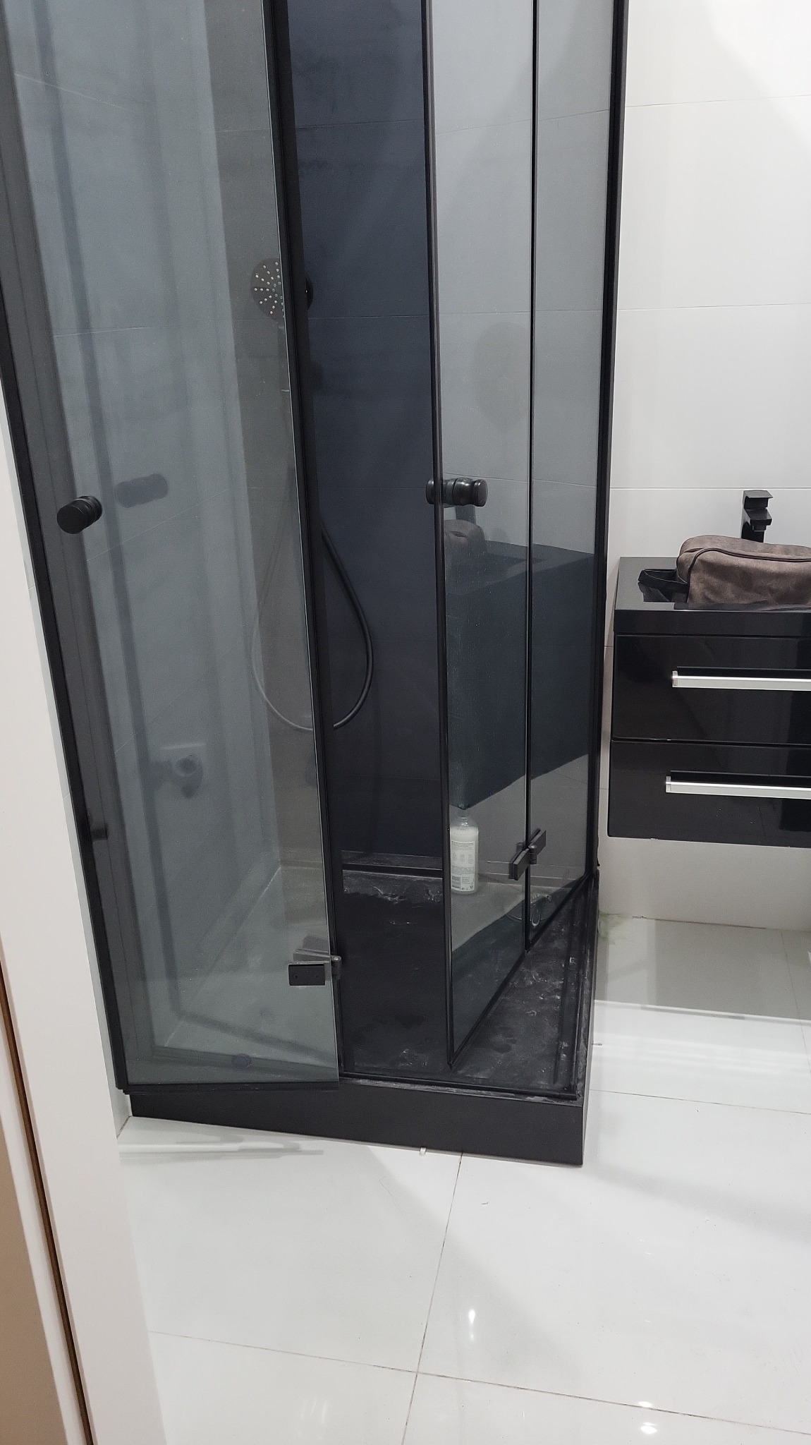 Nowoczesna kabina prysznicowa z czarnymi profilami i grafitowym szkłem, uzupełniona czarną szafką z umywalką. Minimalistyczny design łazienki.
