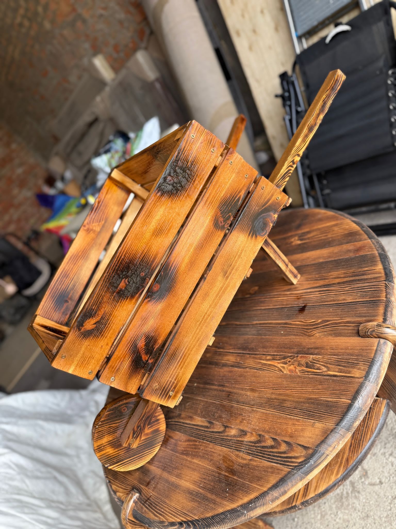 Ręcznie wykonana, opalana skrzynka na drewnianym, okrągłym stole z widocznymi słojami. Unikalne wykończenie, rustykalny styl.