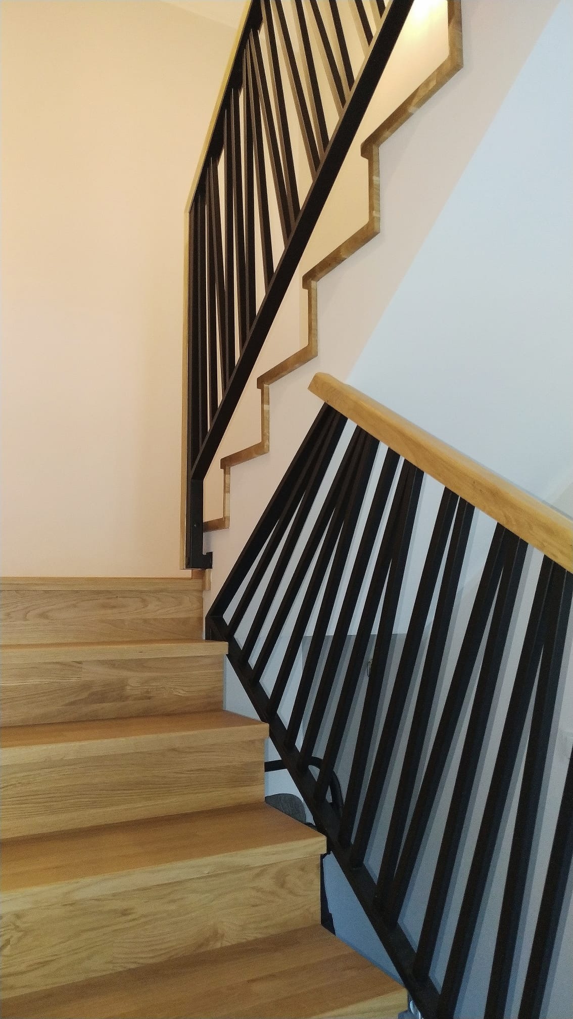 Nowoczesne schody drewniane z czarną metalową balustradą i jasną poręczą, widok z dołu. Minimalistyczny design, jasne wnętrze.