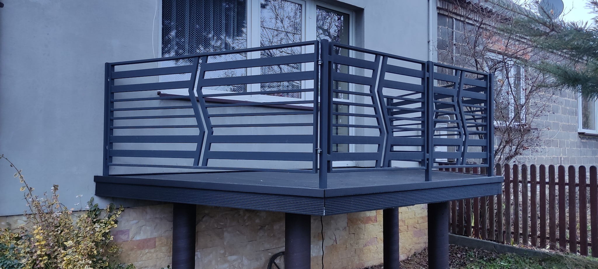 Szara, nowoczesna balustrada balkonowa z poziomych profili, z geometrycznym wzorem, na tle elewacji budynku. Widok z dołu, oświetlenie dzienne.