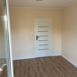 Mateusz Waligóra - Jasne wnętrze po remoncie: drewnopodobne panele, białe listwy przypodłogowe i drzwi z poziomymi przeszkleniami. Nowoczesna lampa sufitowa.