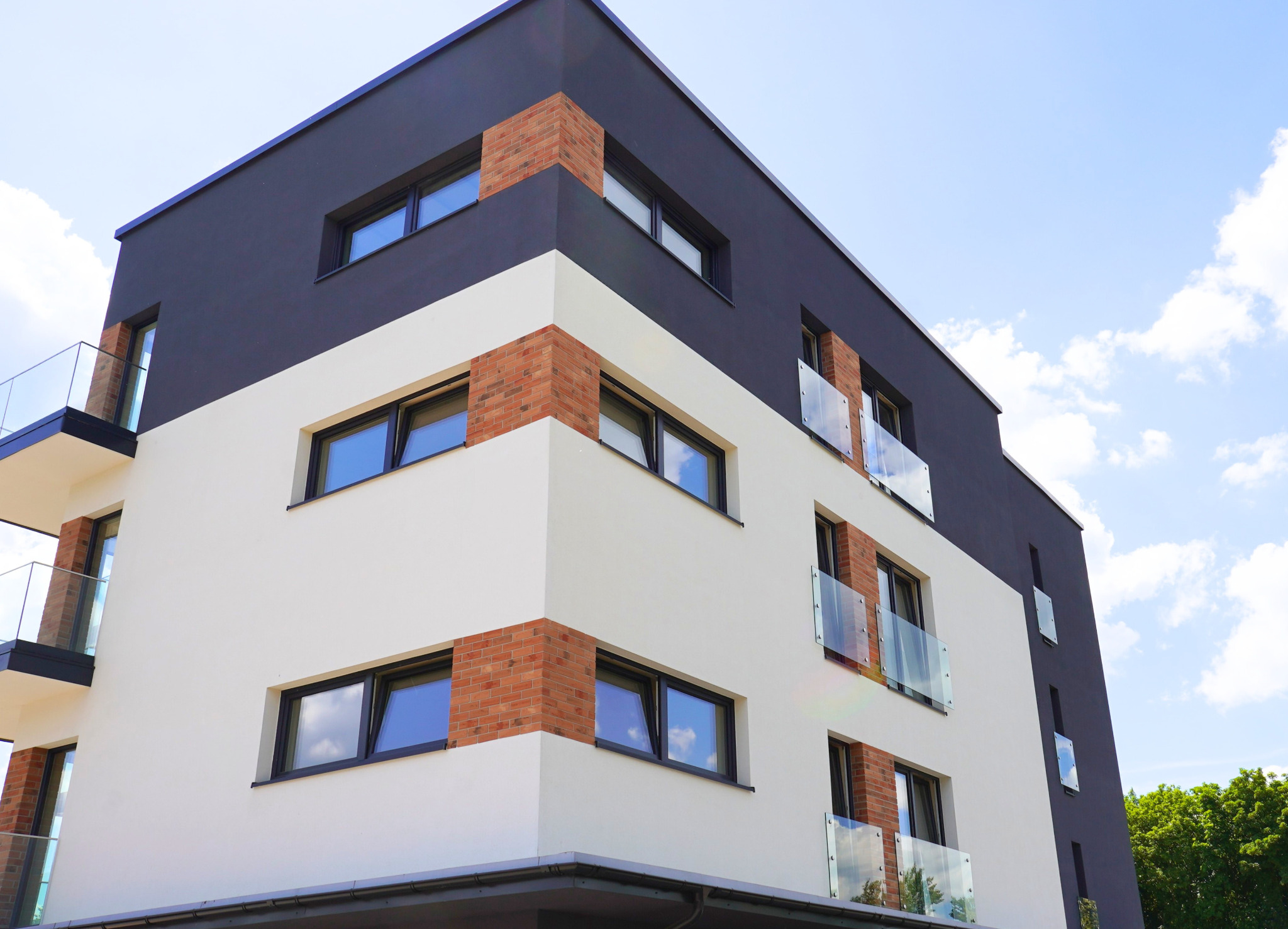 Nowoczesny budynek wielorodzinny z oknami w czarnych ramach i balkonami ze szklanymi balustradami w Tarnowskich Górach. Elewacja w kolorach bieli i grafitu.