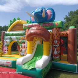 Kolorowy dmuchany park rozrywki Safari Park z motywami zwierzęcymi, zjeżdżalnią i postaciami zwierząt, ustawiony na trawie w plenerze, w tle drzewa.