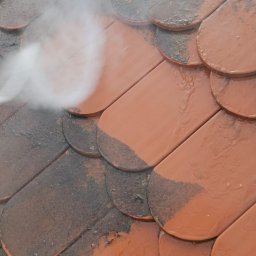 PROCLEAN360 Grzegorz Pikuła - Częściowo umyty dach z dachówki karpiówki w Skoczowie. Strumień wody pod ciśnieniem usuwa zabrudzenia, ukazując czystą, czerwoną powierzchnię. Widoczna para wodna.