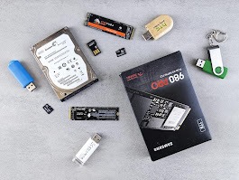 Różne nośniki danych: dysk HDD, SSD M.2, pendrive, karty pamięci microSD, pudełko dysku SSD Samsung 980 PRO, kluczyk USB. Jasne tło, ujęcie z góry.