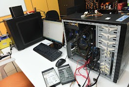 Otwarta obudowa komputera stacjonarnego z widocznymi podzespołami, dyski twarde na biurku, monitor i klawiatura w tle. Sprzęt w serwisie.