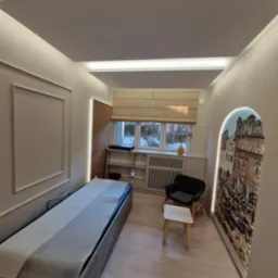 Jasne wnętrze gabinetu z łóżkiem do masażu, krzesłem i dekoracyjną fototapetą w kształcie łuku. Subtelne oświetlenie LED podkreśla nowoczesny charakter.