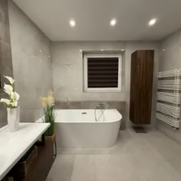 Elegancka łazienka w odcieniach szarości z wolnostojącą wanną, umywalką na blacie i grzejnikiem drabinkowym. Minimalistyczny wystrój z akcentami roślinnymi.