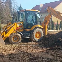Mar-Bud - Żółta koparko-ładowarka JCB na placu budowy, w tle dom i drzewa. Maszyna przygotowuje teren pod budowę, widoczna świeżo przekopana ziemia.