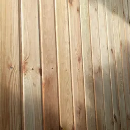 Świeżo zamontowana boazeria z jasnego drewna, widoczne słoje i gwoździe. Ułożenie pionowe desek tworzy ciepły, naturalny wygląd ściany.