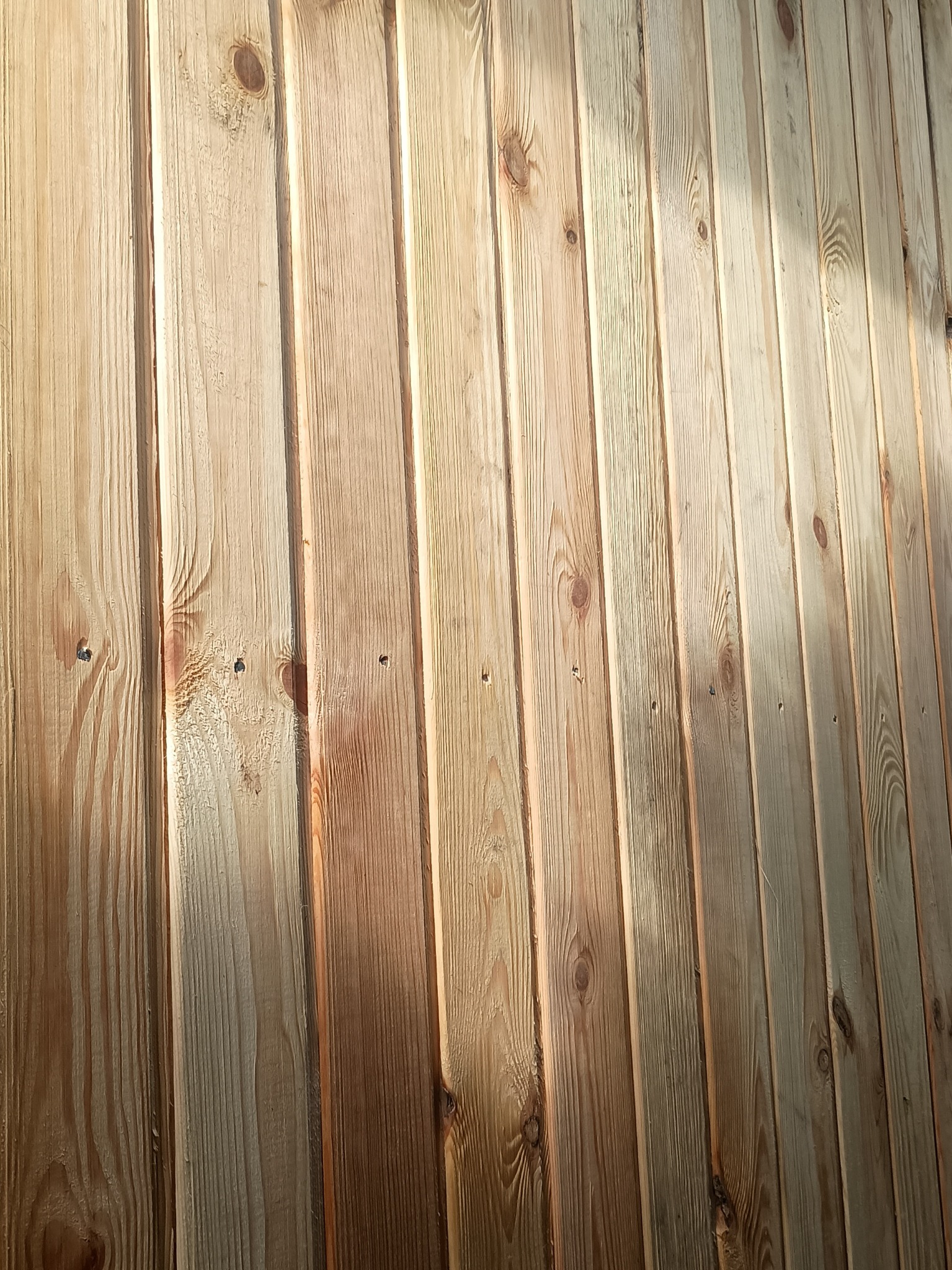 Świeżo zamontowana boazeria z jasnego drewna, widoczne słoje i gwoździe. Ułożenie pionowe desek tworzy ciepły, naturalny wygląd ściany.