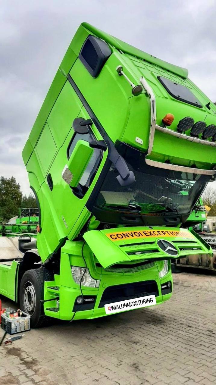 Otwarta kabina zielonej ciężarówki Mercedes z napisem 'CONVOI EXCEPTION' i hasztagiem #WIALONMONITORING na zderzaku. Widoczne narzędzia obok pojazdu.
