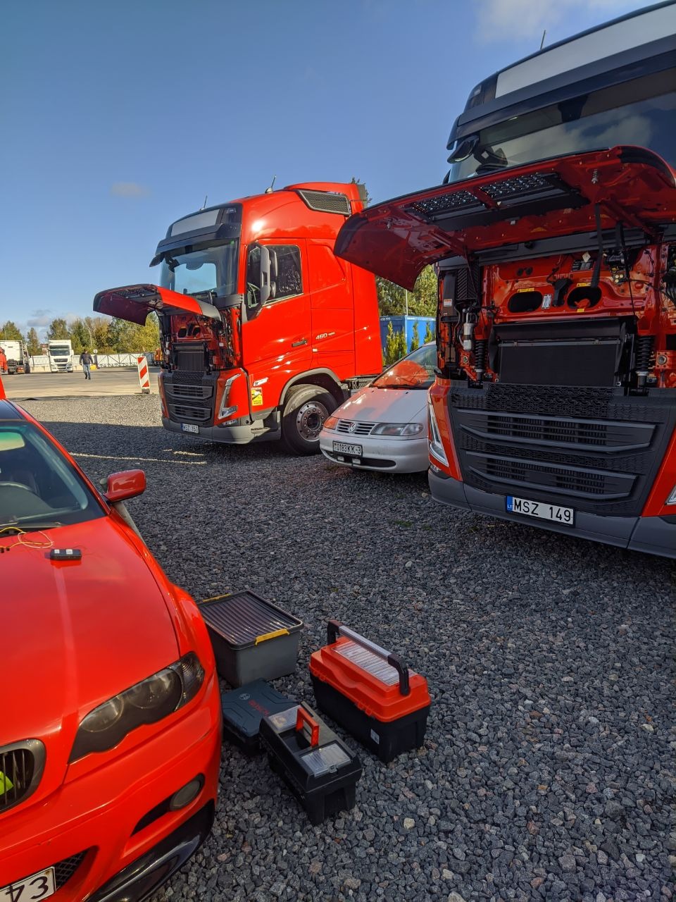 Czerwone ciężarówki z otwartymi maskami na żwirowym placu, narzędzia obok auta. Monitoring GPS - lokalizacja pojazdów i analiza danych.