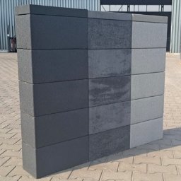 BRUKSTONE SPÓŁKA Z OGRANICZONĄ ODPOWIEDZIALNOŚCIĄ - Prezentacja różnorodności faktur i kolorów na prefabrykowanych elementach betonowych ułożonych w kolumnę. Widoczne detale powierzchni i subtelne różnice w odcieniach szarości.