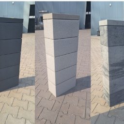 BRUKSTONE SPÓŁKA Z OGRANICZONĄ ODPOWIEDZIALNOŚCIĄ - Trzy słupki ogrodzeniowe z betonowych bloczków o różnych kolorach i fakturach, ustawione na kostce brukowej. Tło stanowi blaszany budynek.