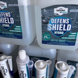 BRUKSTONE SPÓŁKA Z OGRANICZONĄ ODPOWIEDZIALNOŚCIĄ - Impregnat i klej do betonu Defens Shield Hydro w białych opakowaniach, przeznaczone do ochrony ogrodzeń betonowych i kostki brukowej, widoczne etykiety z opisem produktu.