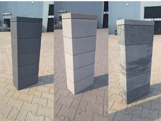Trzy słupki ogrodzeniowe z betonowych bloczków o różnych kolorach i fakturach, ustawione na kostce brukowej. Tło stanowi blaszany budynek.