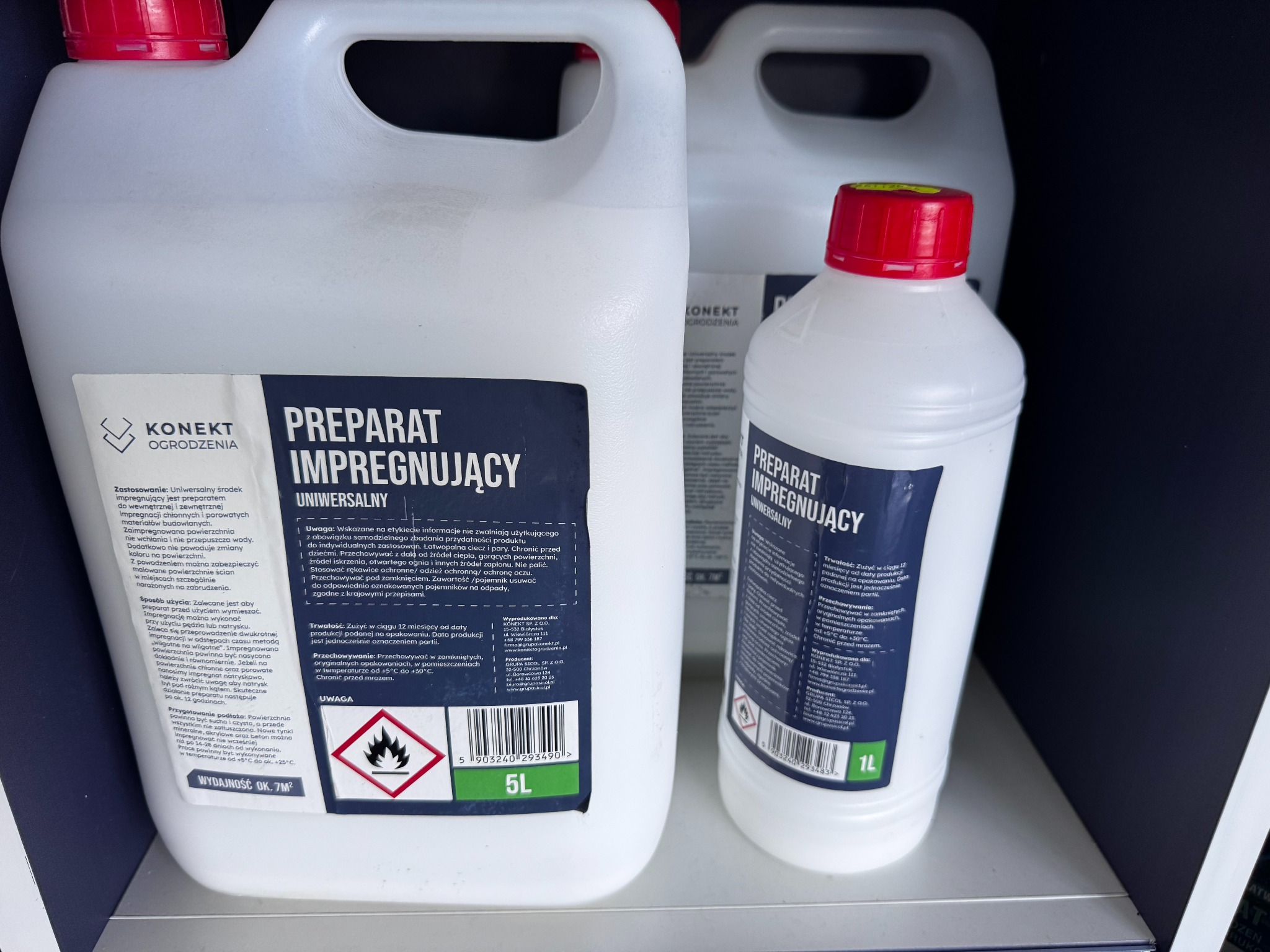 Białe kanistry z preparatem impregnującym marki Konekt Ogrodzenia na półce. Jeden kanister 5L, drugi 1L. Widoczne etykiety z informacjami o produkcie.