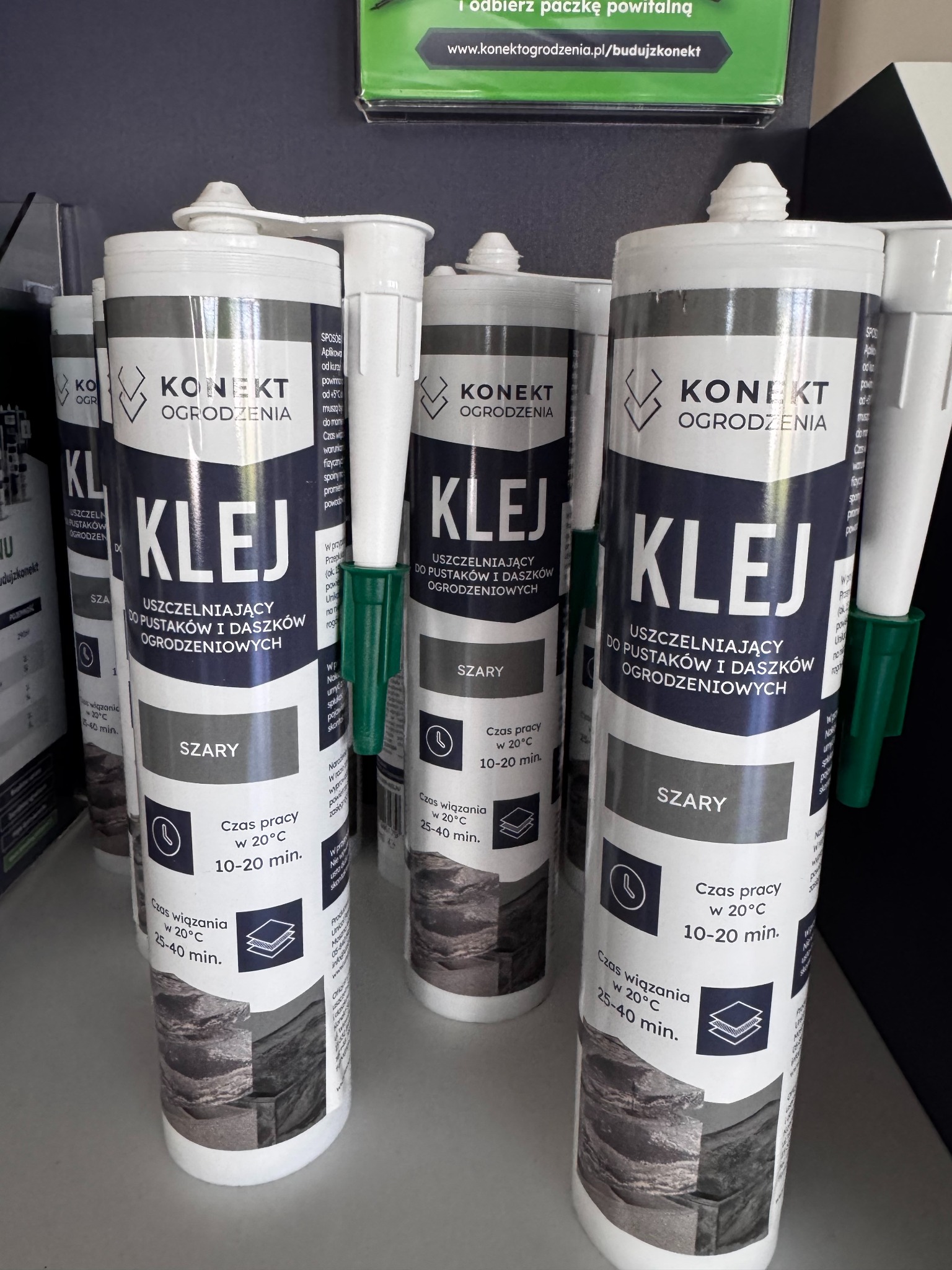Klej uszczelniający do pustaków i daszków ogrodzeniowych marki Konekt Ogrodzenia, w szarym kolorze, z informacją o czasie pracy i wiązania. Prezentacja produktu na półce.