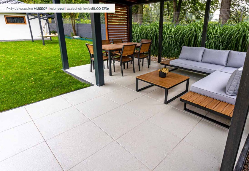 Jasnoszara, kwadratowa kostka betonowa Musso Opal ułożona na tarasie. W tle meble ogrodowe i zieleń. Uzupełnienie SILCO Elite.