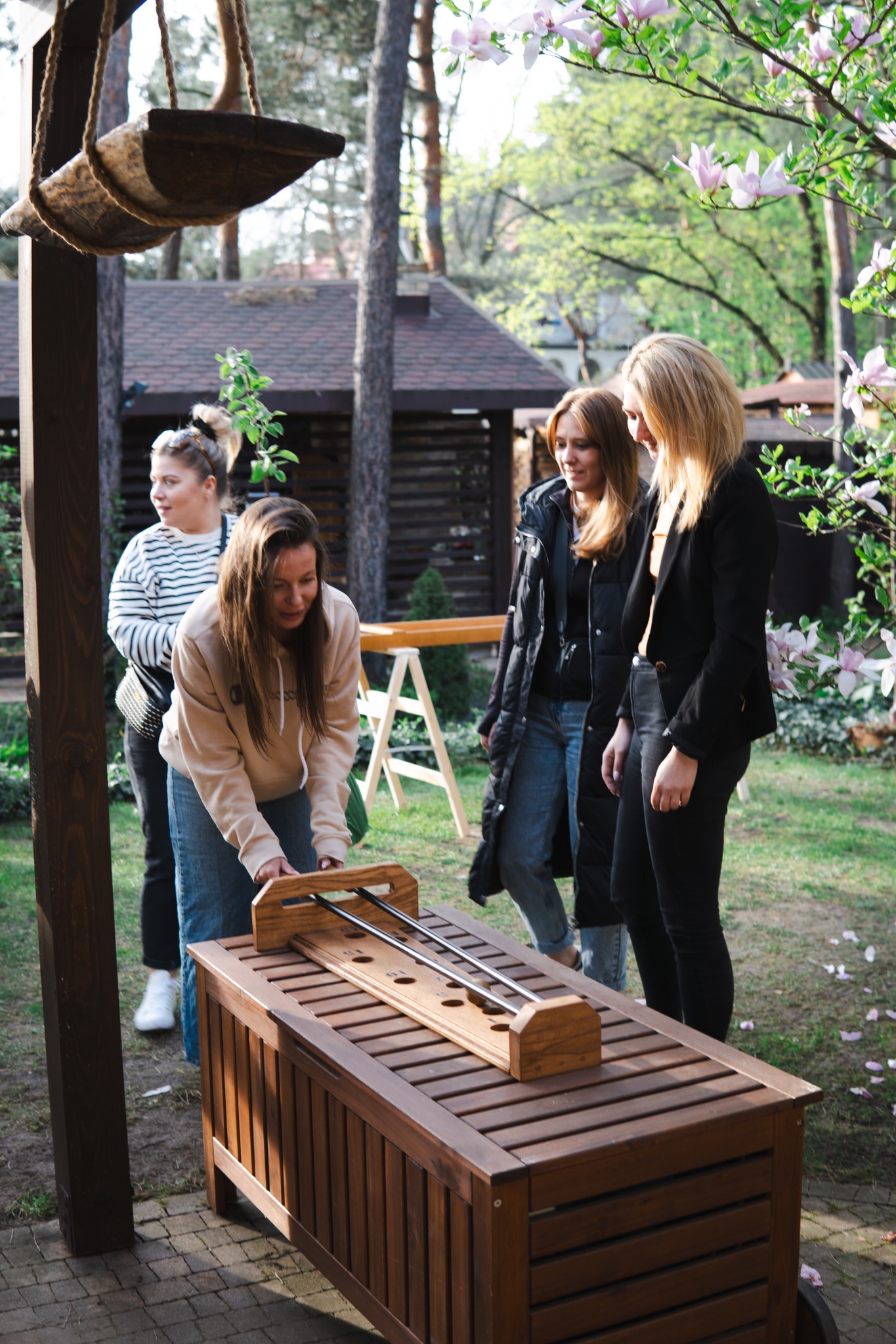 Gra plenerowa na drewnianym stole z grupą kobiet w ogrodzie, magnolia w tle. Aktywność na świeżym powietrzu podczas imprezy, gra zręcznościowa.