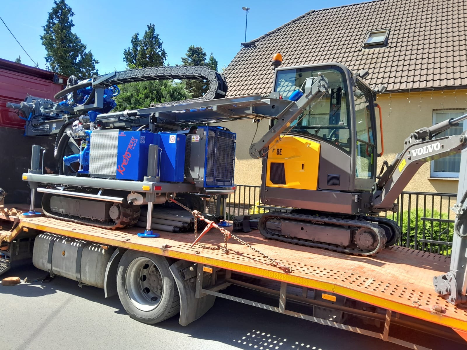 Mobilna wiertnica Kreto MAX na lawecie, obok żółto-szara koparka Volvo, przygotowane do wiercenia otworów pod gruntowe wymienniki ciepła.