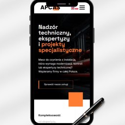 PaolaProject - Ekran smartfona prezentuje stronę internetową firmy APCAS z hasłem 'Nadzór techniczny, ekspertyzy i projekty specjalistyczne'. Obok leży czarny długopis.